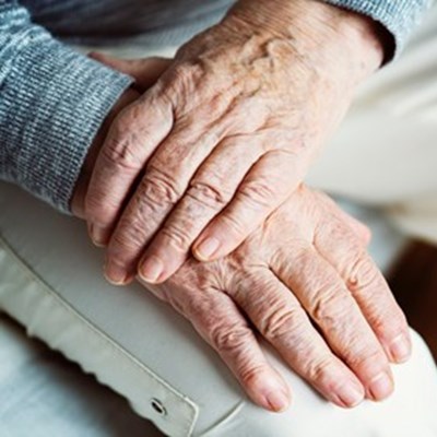 Et par hænder på en ældre person. Personen holder sit ene håndled med den anden hånd.
